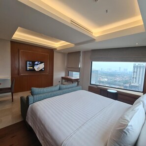A modern hotel room with a large bed, a seating area, a television, and a city view. - Trembesi Hotel BSD (South Tangerang)