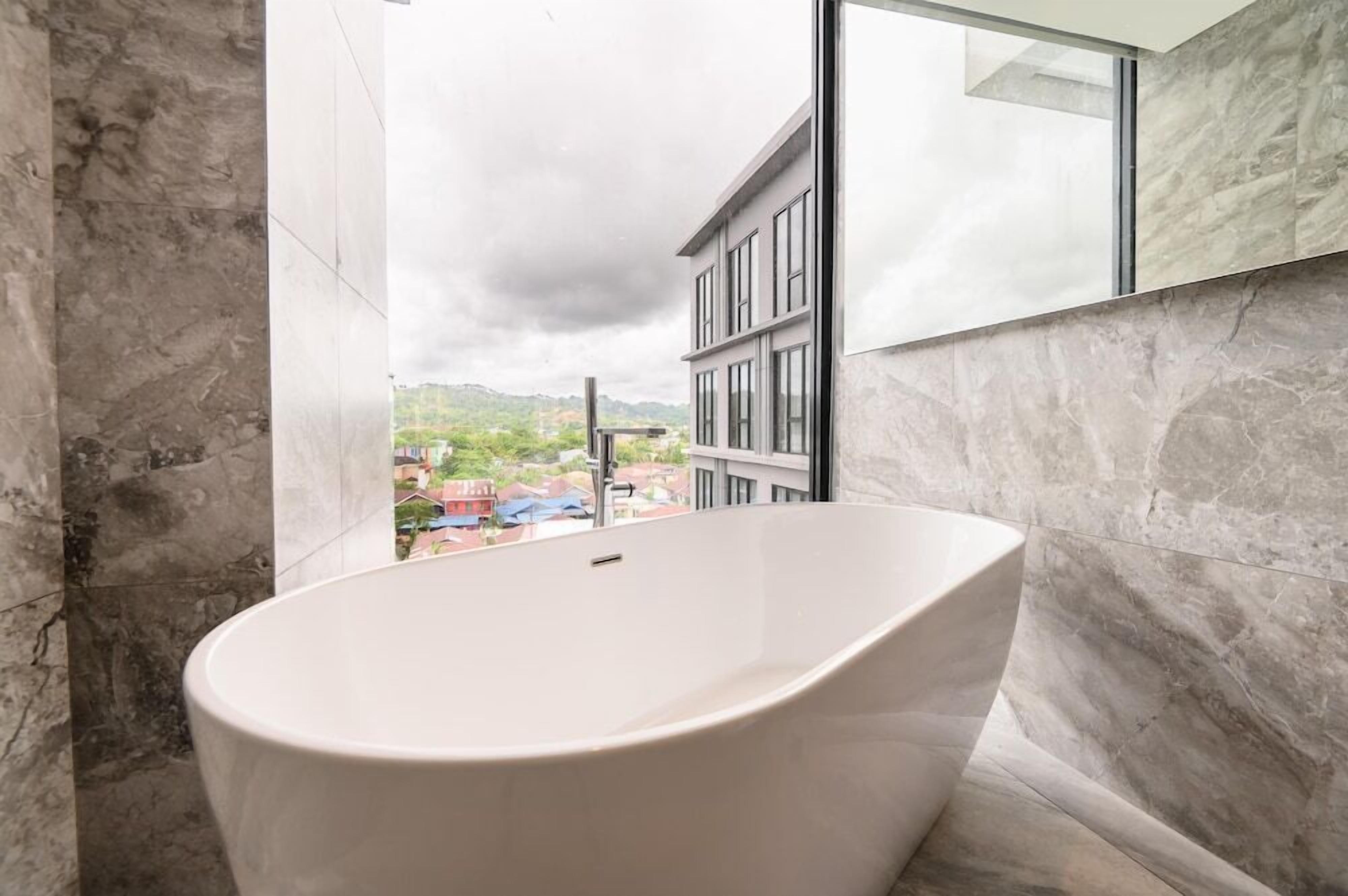 Un baño moderno con una bañera independiente, ventanas amplias y vistas a la ciudad.