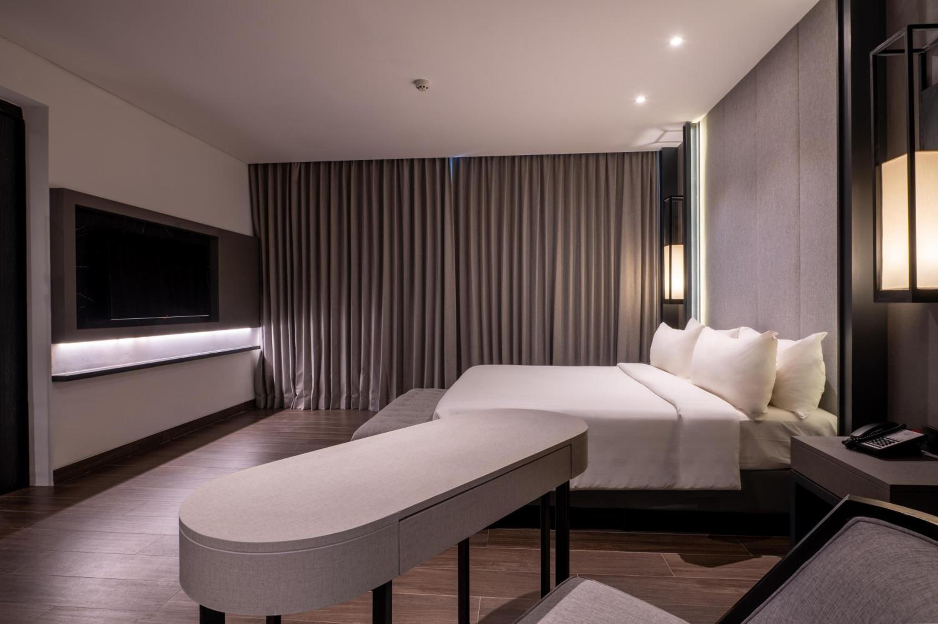 A modern hotel room with a bed, bedside table, and a flat-screen TV mounted on the wall.