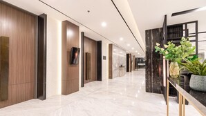 A modern hotel lobby with a marble floor, wooden paneling, a reception desk, and a large vase with plants. - Aston Sorong Hotel and Conference Center (Sorong)