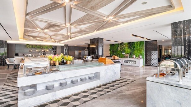 A modern hotel lobby with a central reception desk, a bar area, and a green wall with plants. - Aston Sorong Hotel and Conference Center (Sorong)