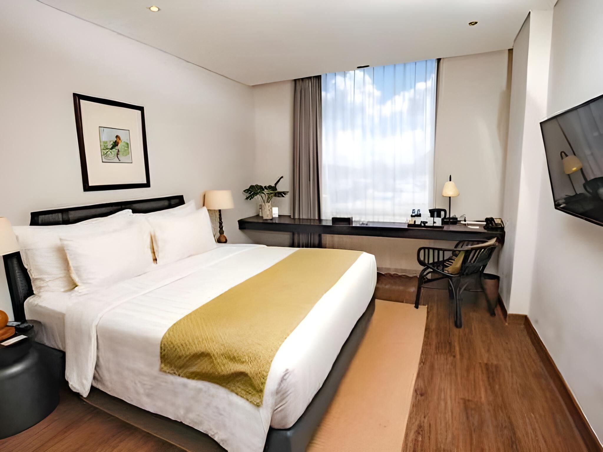Una habitación de hotel con cama, escritorio, silla y televisor en la pared.