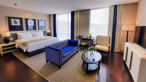Une chambre d’hôtel avec un lit, un canapé bleu, une petite table avec un vase, une chaise et un téléviseur.