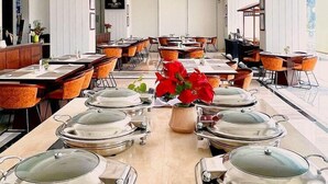 Un vaste espace dédié à la salle à manger, avec de longues tables, des chaises modernes et une plante décorative placée au centre.