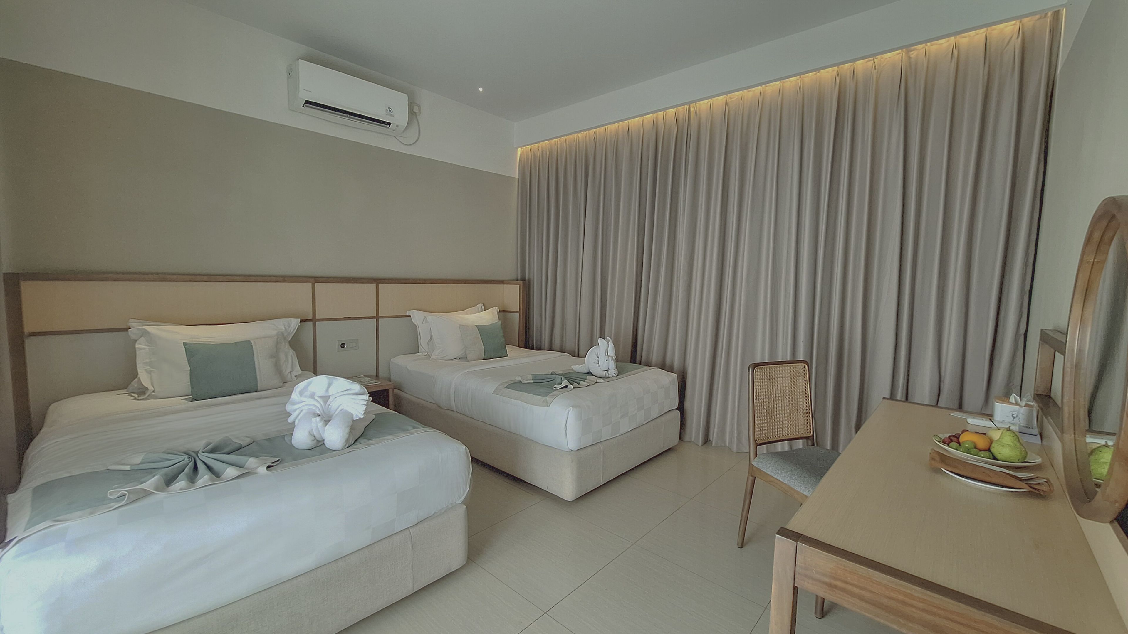 Habitación de hotel con dos camas, un escritorio, una silla y un amplio ventanal con cortinas.