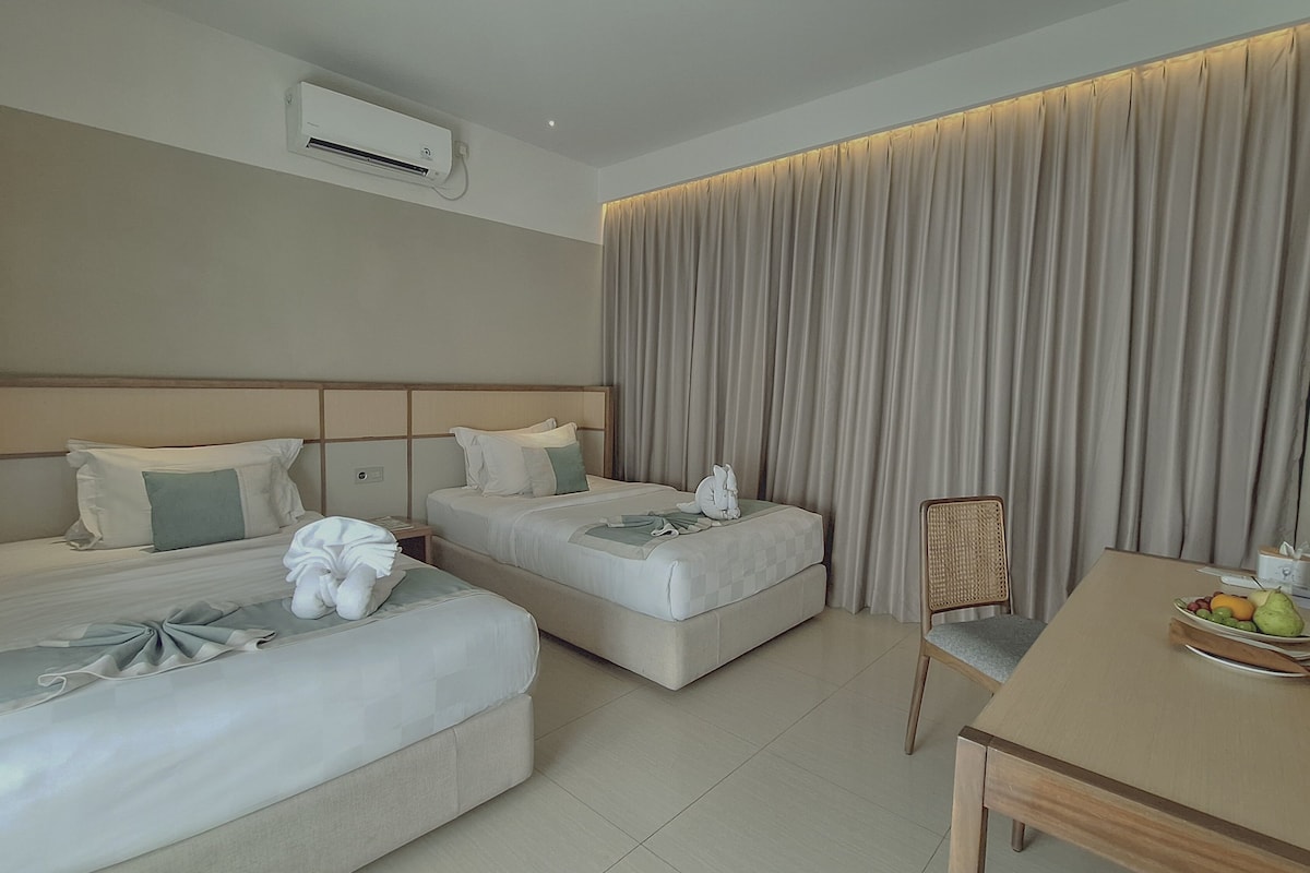 A hotel room with two beds, a desk, a chair, and a large window with curtains.