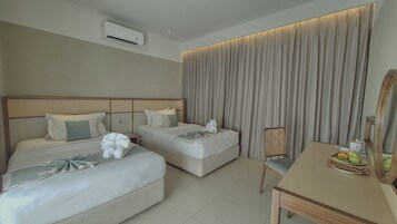 Habitación de hotel con dos camas, un escritorio, una silla y un amplio ventanal con cortinas.