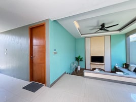 Una sala de estar moderna con puerta de madera, ventilador de techo, televisor de pantalla plana, zona de estar con sofá y planta en maceta.