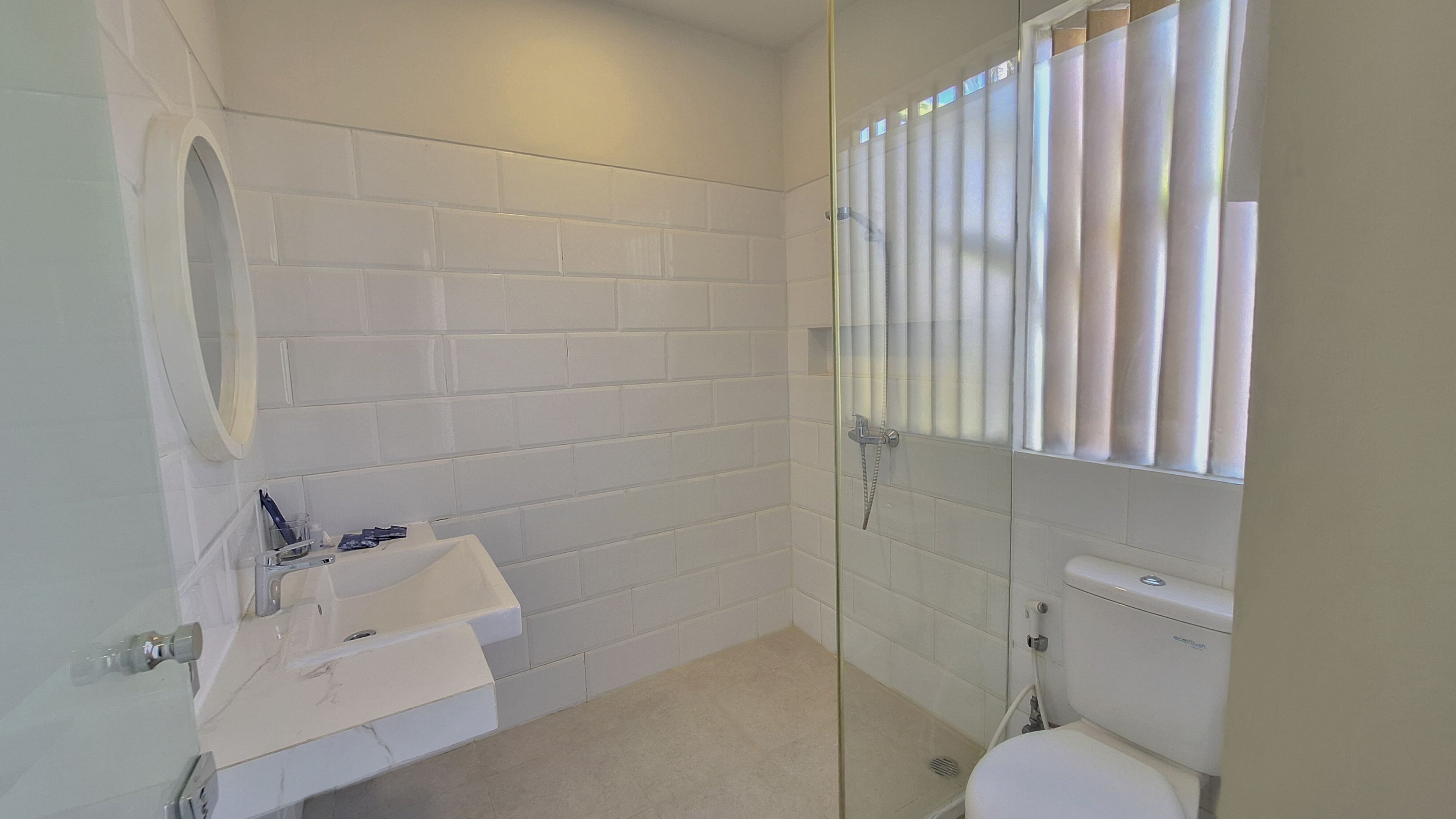 Een badkamer met een wit betegelde muur, een glazen douchecabine, een witte wastafel en een toilet.