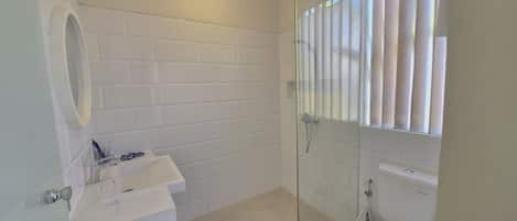 A bathroom with a white tiled wall, a glass shower enclosure, a white sink, and a toilet.