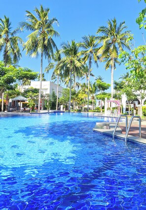 A swimming pool surrounded by palm trees and a building with a white facade. - The Allure Villas Managed by Sahid (Pangandaran)