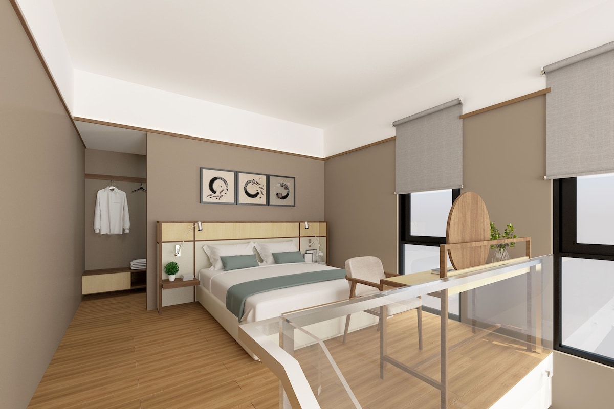 A modern hotel room with a bed, bedside table, and a desk with a chair.
