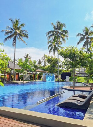 A swimming pool with a slide, surrounded by palm trees and lounge chairs. - The Allure Villas Managed by Sahid (Pangandaran)