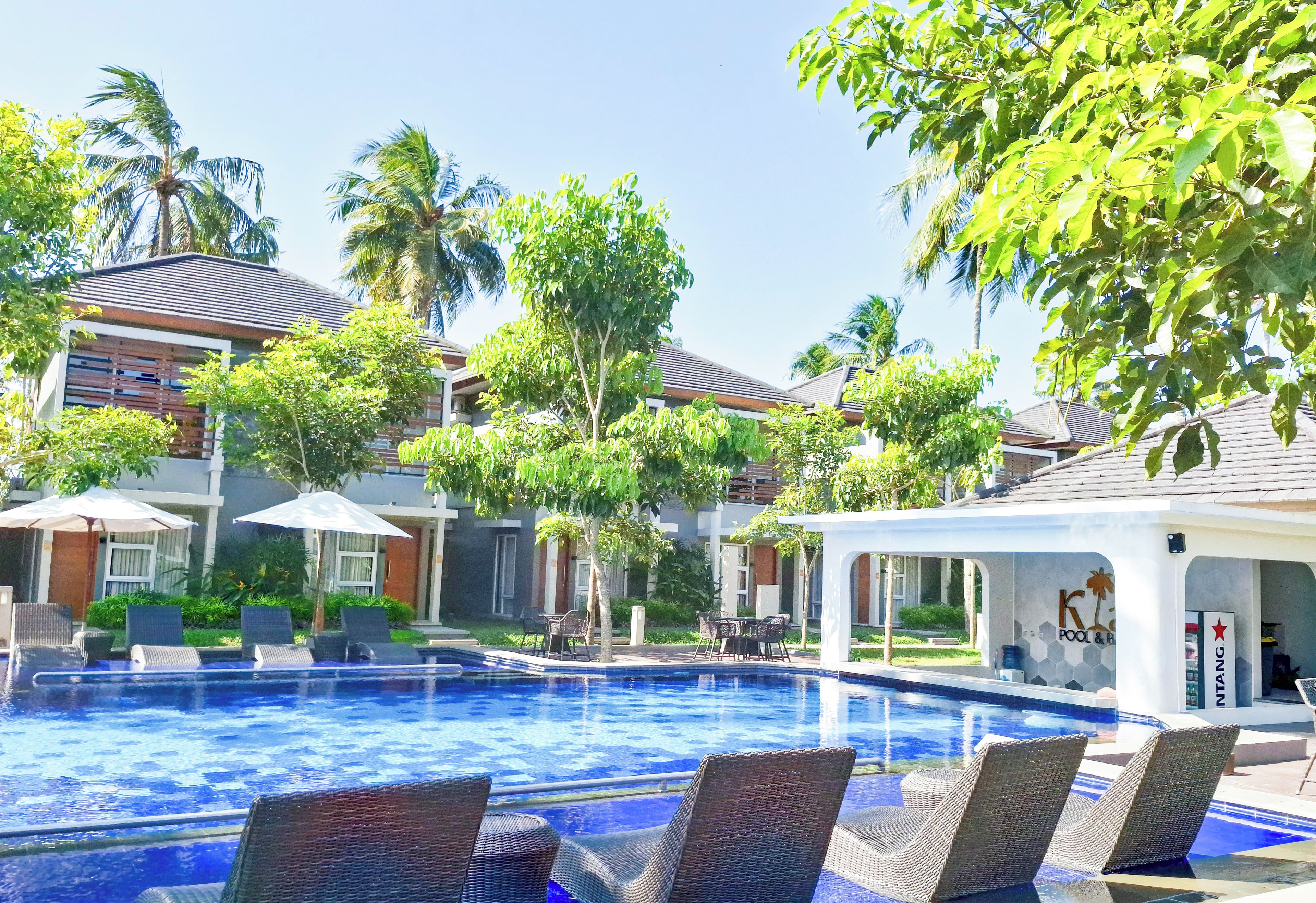 Ein Swimmingpool mit Liegestühlen, Palmen und ein Gebäude mit der Aufschrift 'K Pool & Spa'.