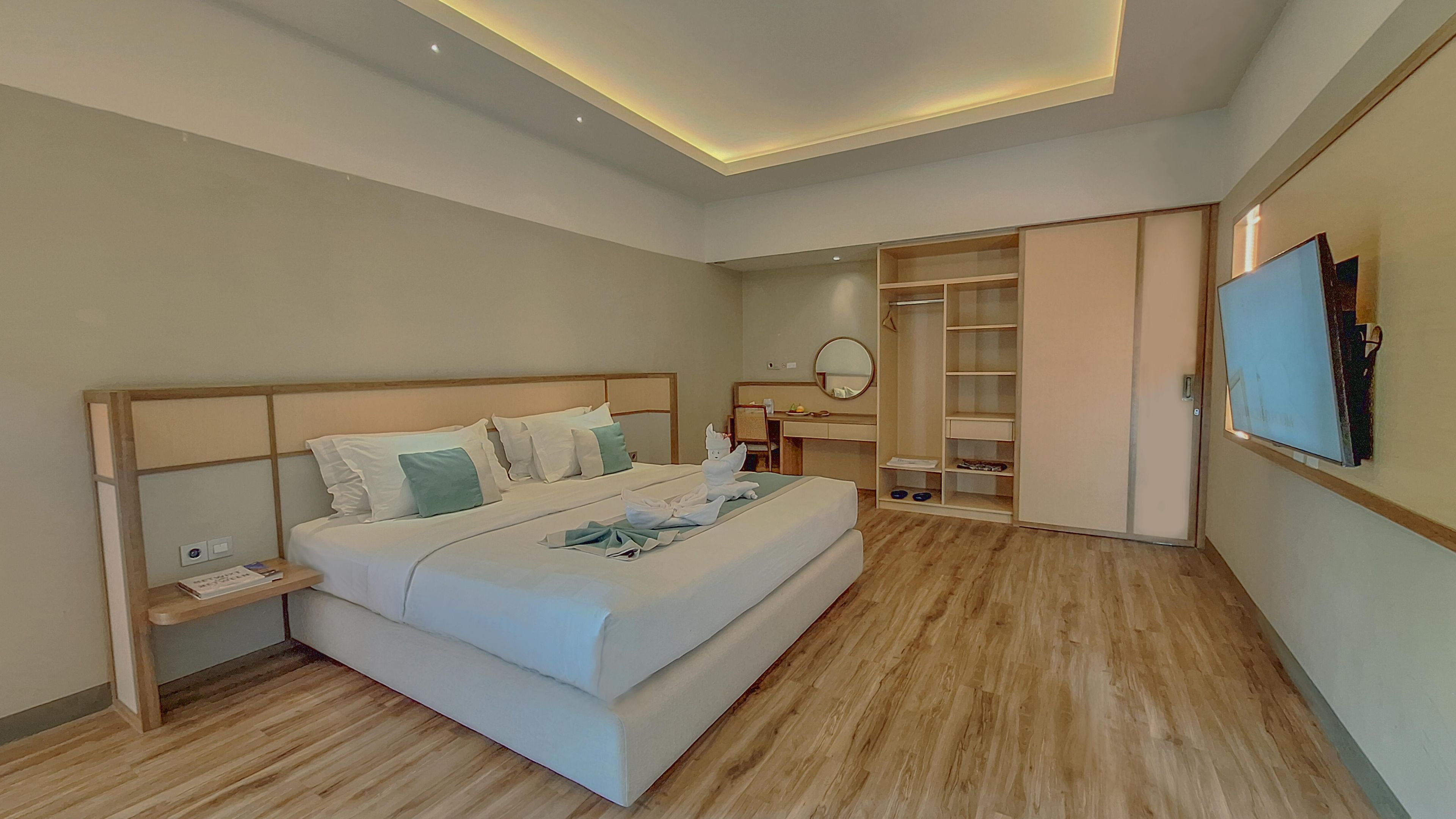 A modern hotel room with a large bed, bedside tables, a desk, a wardrobe, and a TV mounted on the wall.