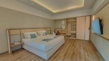 A modern hotel room with a large bed, bedside tables, a desk, a wardrobe, and a TV mounted on the wall.