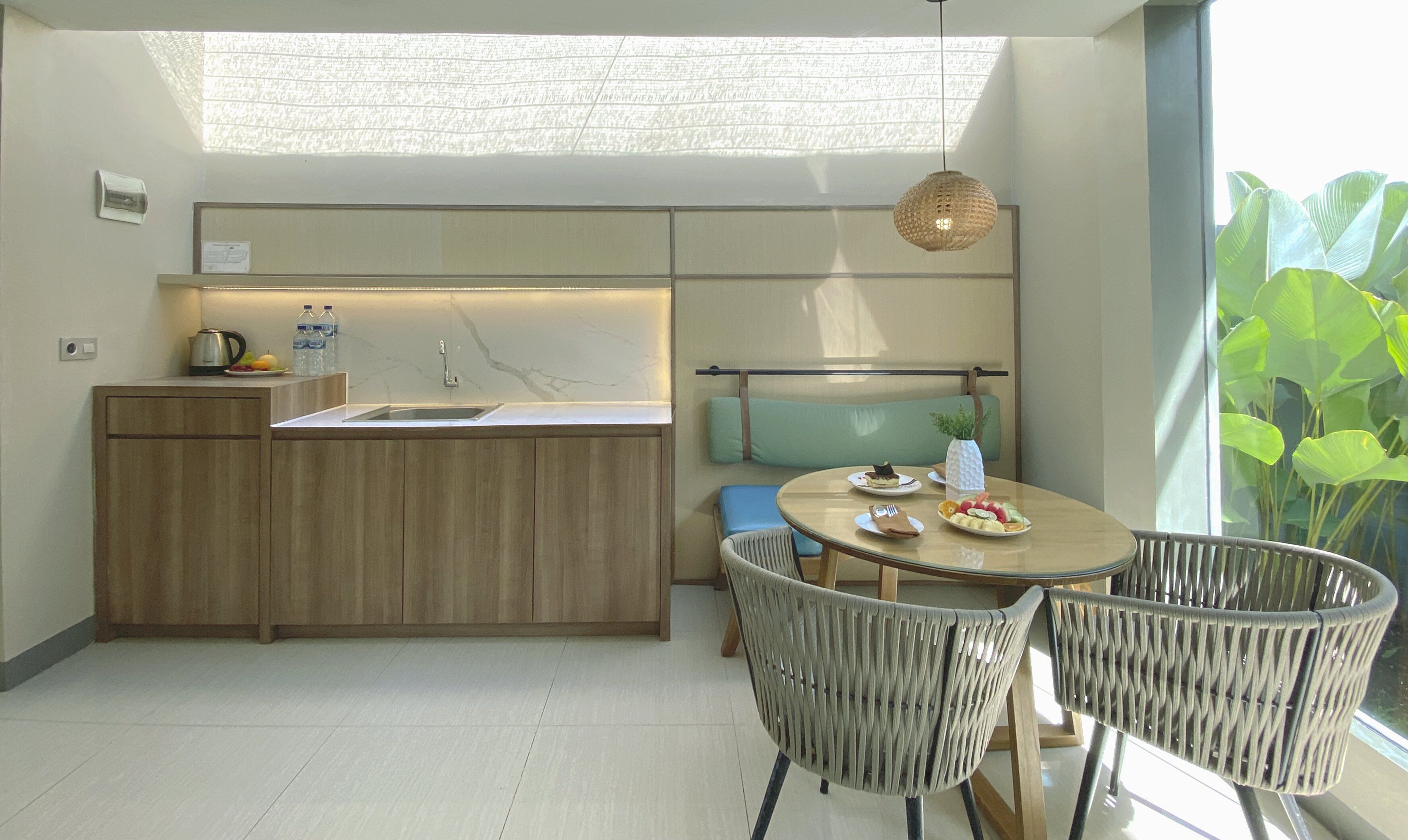 Una cocina moderna con una isla integrada, un área de comedor con sillas de mimbre y un amplio ventanal con vistas a la vegetación.