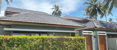 A modern building with a sloped roof, a well-maintained hedge, and palm trees in the background.