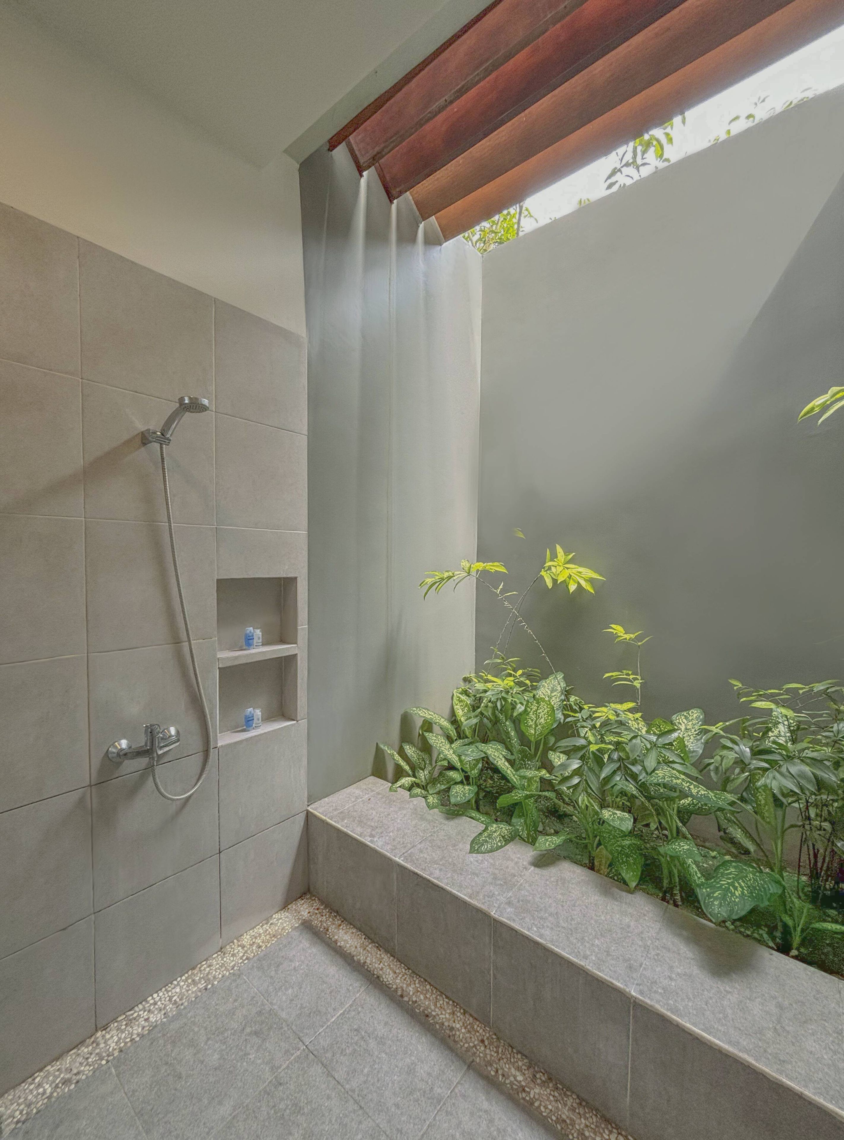 A modern shower area with a rain showerhead, a built-in shelf, and a planter with green foliage.