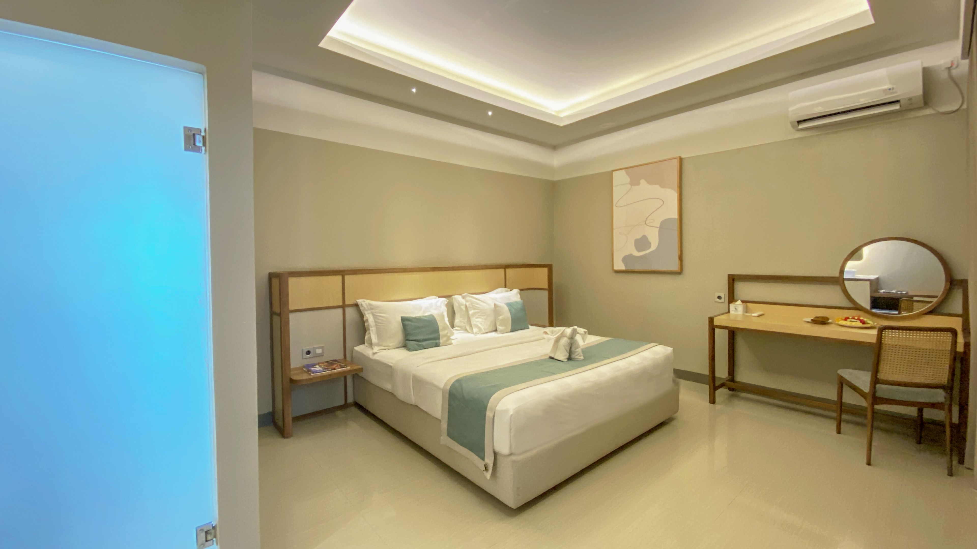 Habitación de hotel con cama, escritorio, silla, espejo y aire acondicionado instalado en la pared.