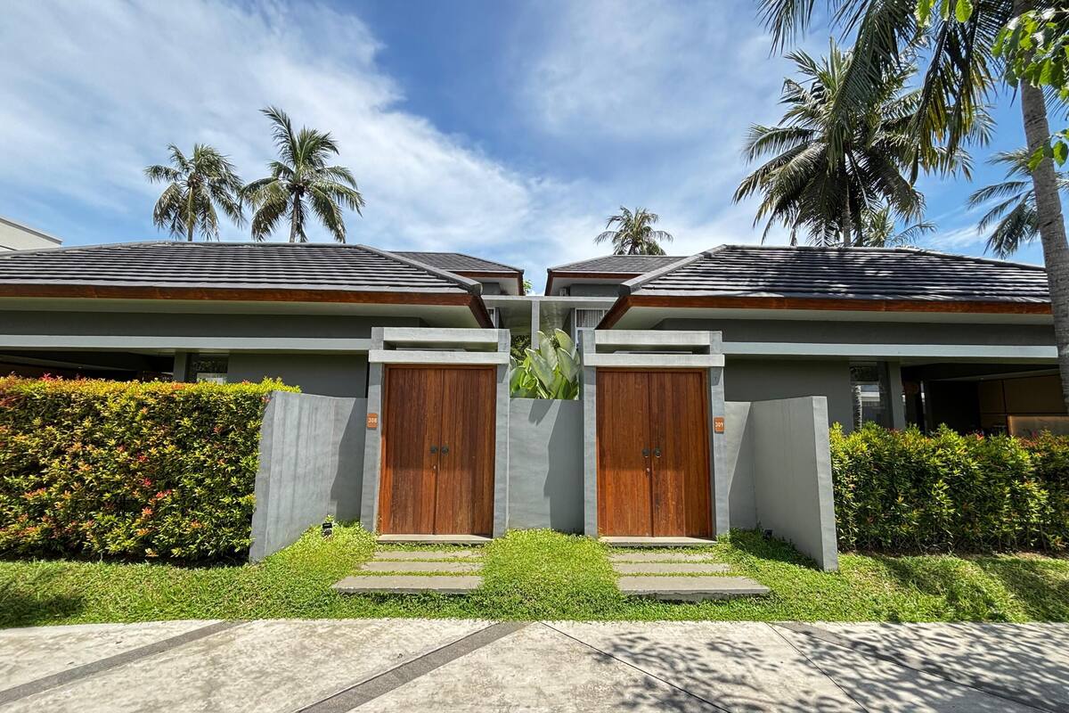 Uma casa moderna de dois andares com fachada de concreto, portas de madeira e um jardim bem cuidado.