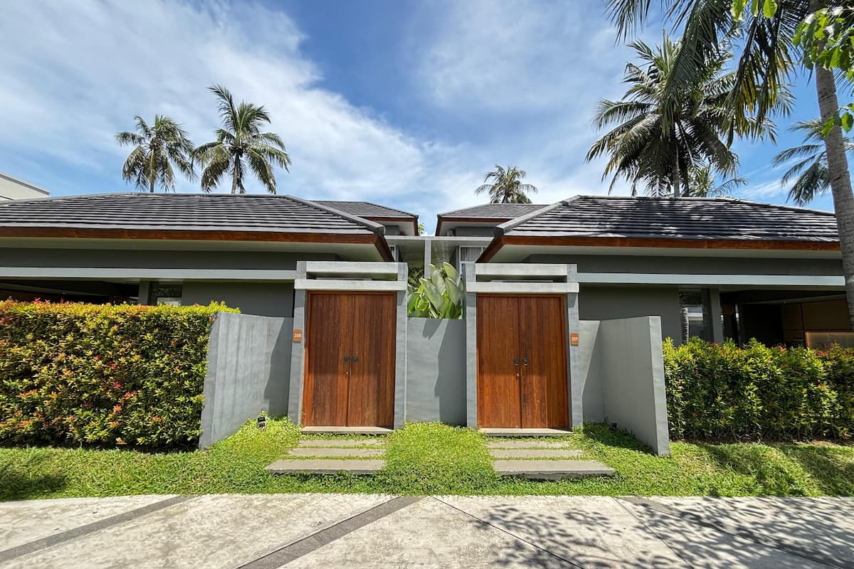 Una casa moderna de dos pisos con fachada de concreto, puertas de madera y un jardín bien cuidado.