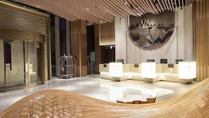A modern hotel lobby with a reception desk, glass doors, and a decorative wall.
