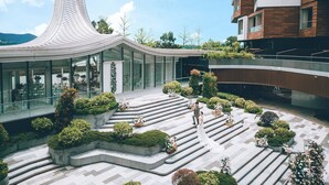 A modern building with a curved roof, a glass facade, and a landscaped courtyard with steps and greenery.