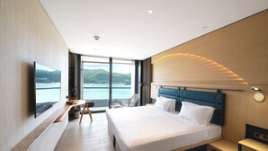 A modern hotel room with a large bed, a desk, a chair, and a TV.