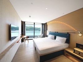 A modern hotel room with a large bed, a desk, a chair, and a TV.