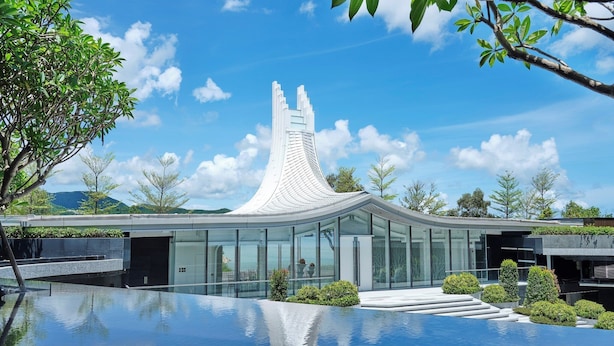 A modern building with a unique curved roof, surrounded by a reflective pool and greenery.