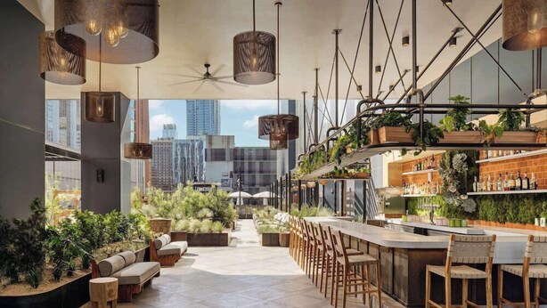 A modern bar area with a long counter, wooden chairs, and hanging plants.