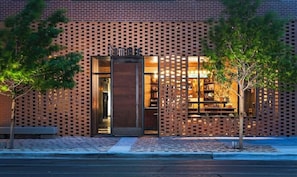 Un bâtiment moderne avec une façade en briques, une entrée en verre et un petit espace extérieur aménagé avec des sièges.