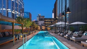 A rooftop pool with lounge chairs and umbrellas, surrounded by modern buildings.