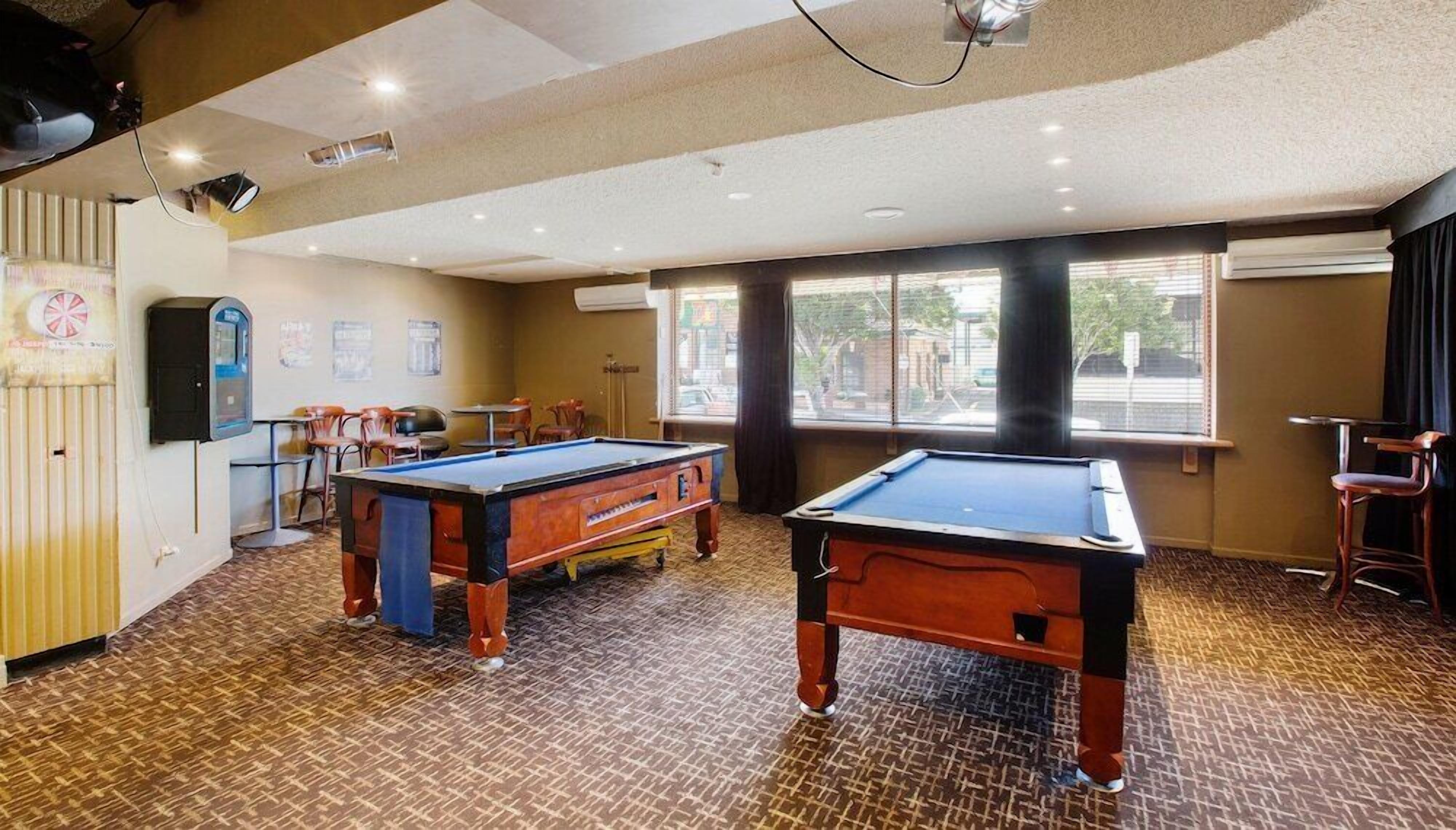 A pool table room with two pool tables, chairs, and a window with a view of the street.