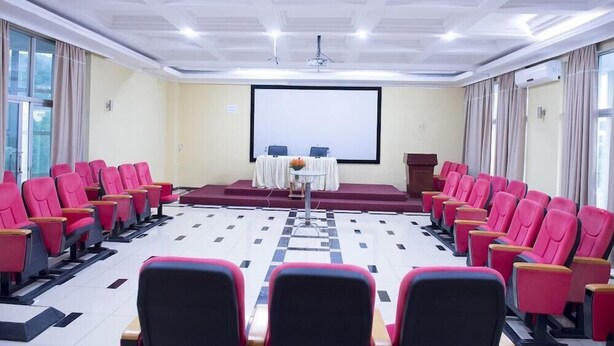 A conference room with a large screen, rows of red chairs, and a stage with a podium. - Martha Hotel Bujumbura (Bujumbura)