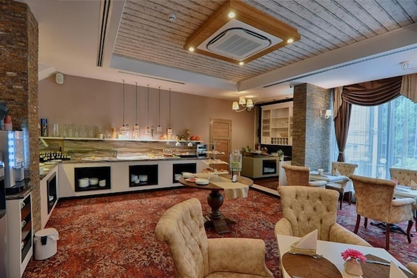 Un vestíbulo de hotel con zona de buffet, arreglos de asientos y un amplio ventanal con vistas.