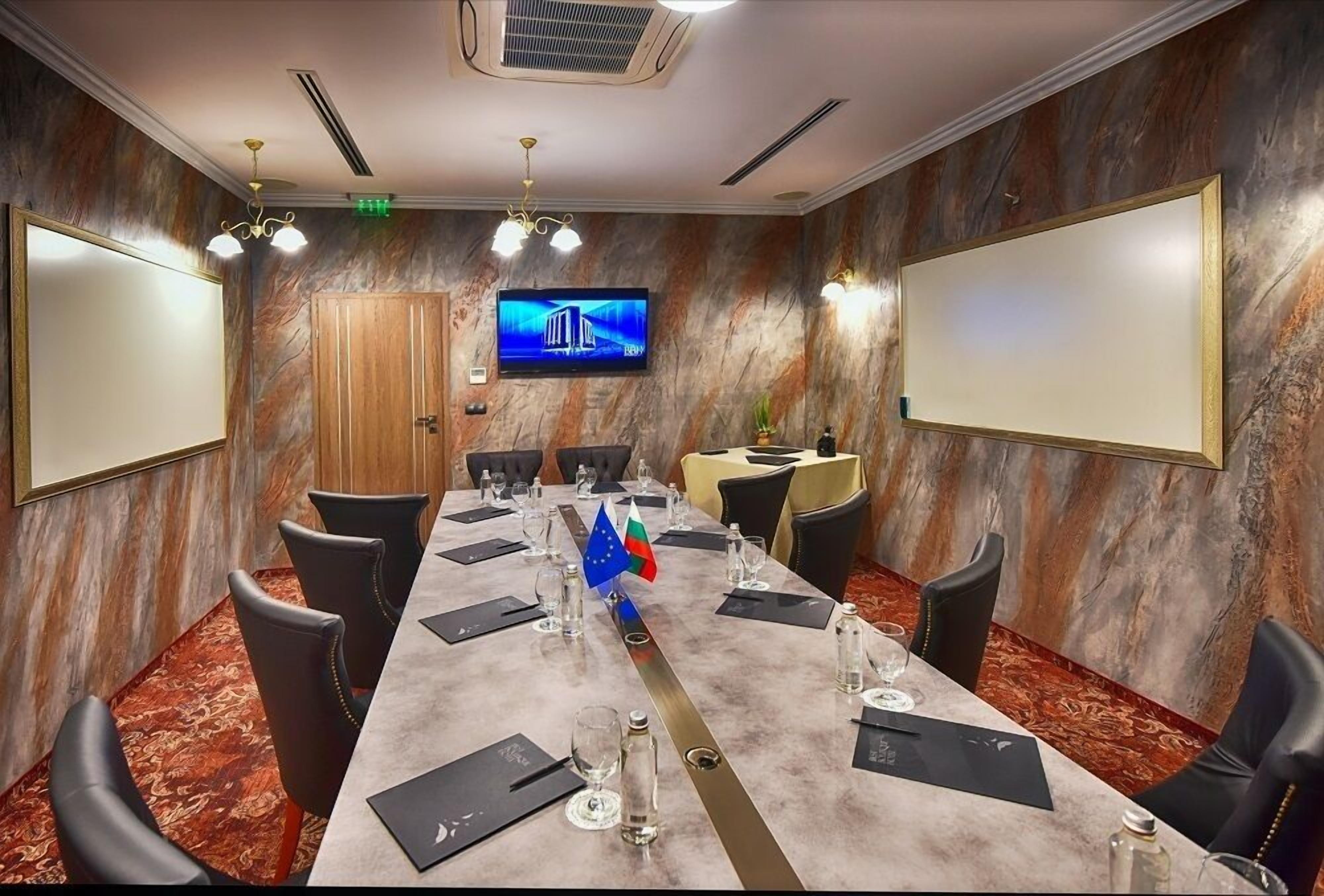Un salón de conferencias con una larga mesa, sillas, un televisor y una bandera.