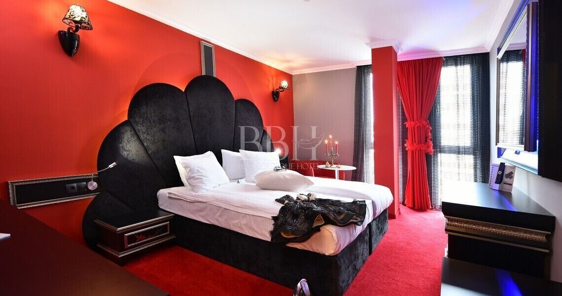 A hotel room with a large bed, a bedside table, a TV, and a window with curtains.