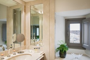 A bathroom with a large mirror, a sink with toiletries, and a potted plant. - Chateau Lafaurie-peyraguey by Lalique (Bommes)