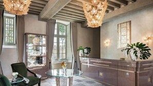 A reception area with a glass-top table, two green chairs, a marble reception desk, and a chandelier. - Chateau Lafaurie-peyraguey by Lalique (Bommes)