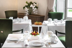 Uma sala de jantar com mesas preparadas para quatro pessoas, toalhas brancas e cadeiras verdes.