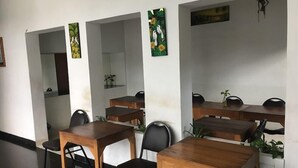 A dining area with wooden tables and black chairs, white walls, and artwork on the walls. - The Nest Hotel by Zuzu (Depok)