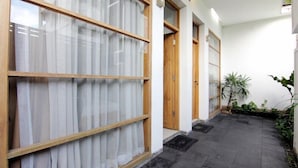 A corridor with wooden-framed windows and doors, a tiled floor, and potted plants. - The Nest Hotel by Zuzu (Depok)