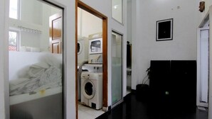 A laundry room with a washing machine and dryer, a mirror, and a door leading to another room. - The Nest Hotel by Zuzu (Depok)