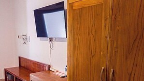 A room with a wooden cabinet, a television mounted on the wall, and a bench. - Ketapang Guest House Canggu by Zuzu (Canggu)