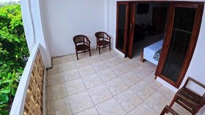 A balcony with tiled flooring, two wooden chairs, a door leading to an interior room, and a view of greenery. - Ketapang Guest House Canggu by Zuzu (Canggu)