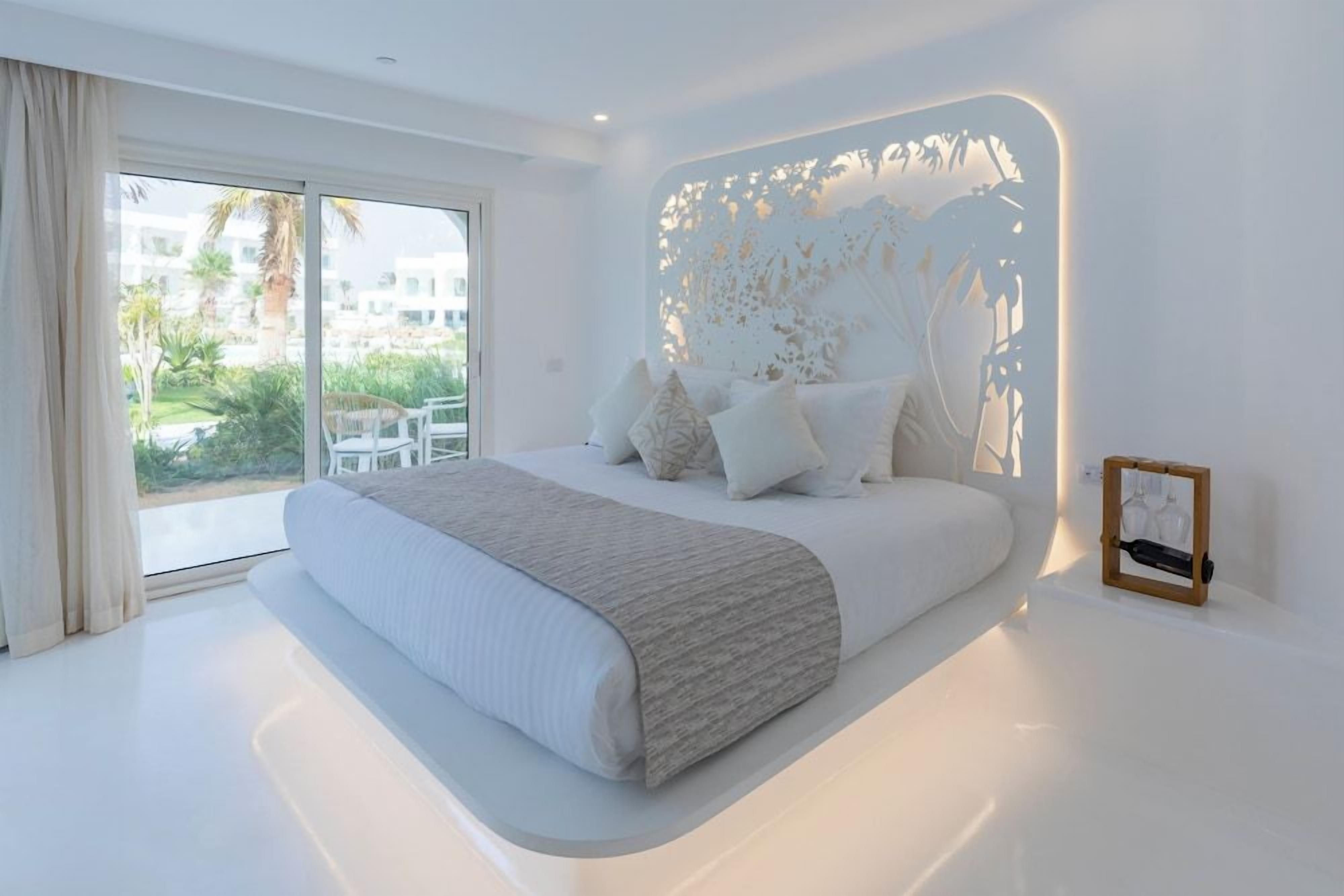 A modern bedroom with a large bed, a view of the outdoors, and a decorative wall panel.