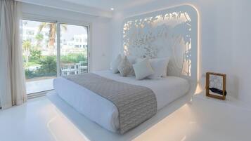 A modern bedroom with a large bed, a view of the outdoors, and a decorative wall panel.