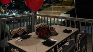 A dining table with four red balloons, a candle, and a vase of flowers on a balcony overlooking a cityscape at night. - The Amman Pasha Hotel (Amman)
